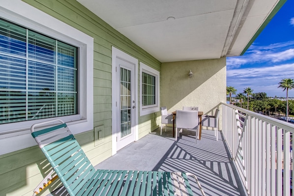 A balcony with a table and chairs, a bench, and a view of palm trees and a clear sky. - New Hotel Collection Harbourside Resort (Indian Rocks Beach)