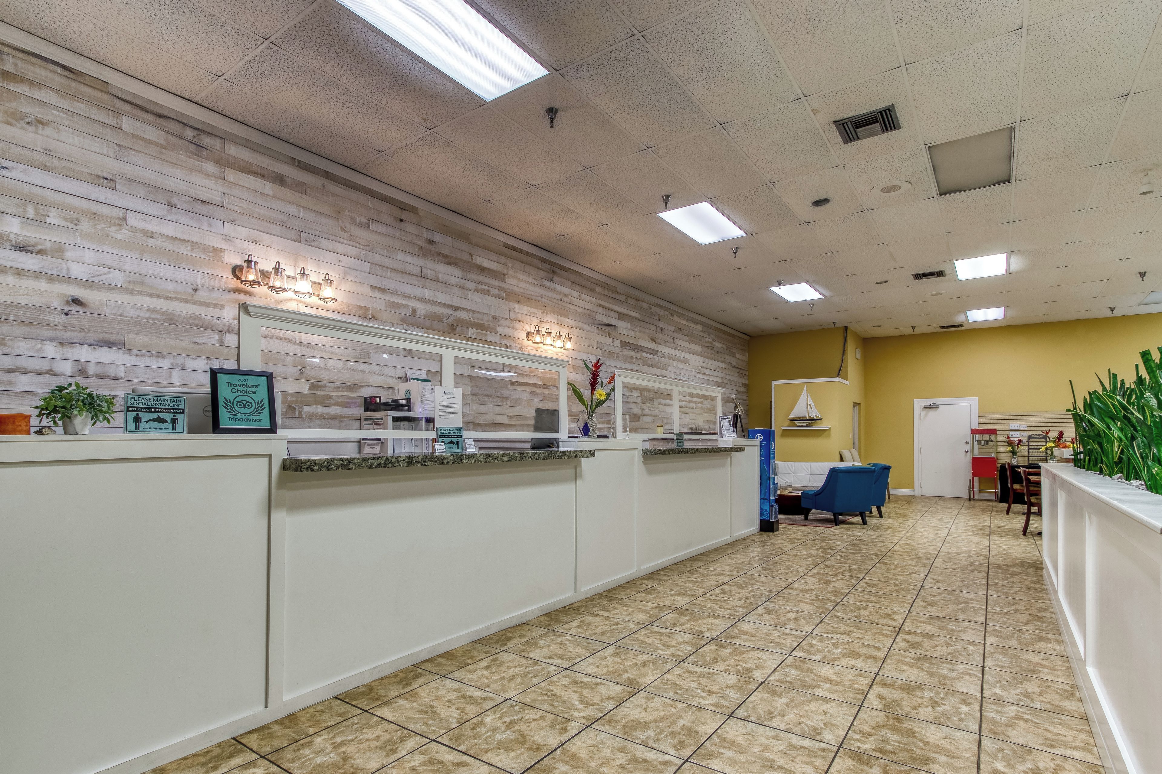 Zona de recepción con suelo de baldosas, mostrador de recepción, una silla azul y pared amarilla.