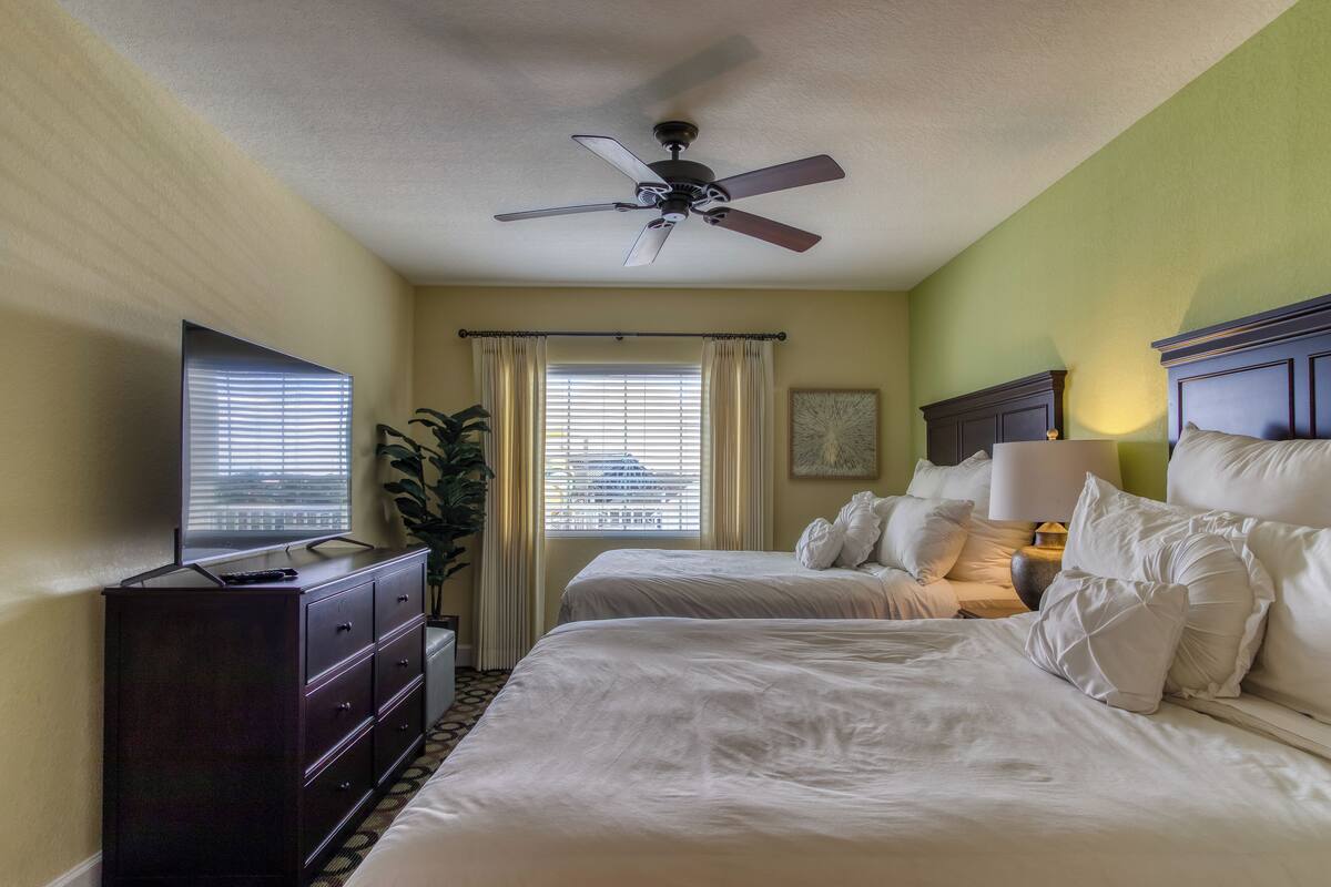 A hotel room with two beds, a ceiling fan, a TV, and a dresser.