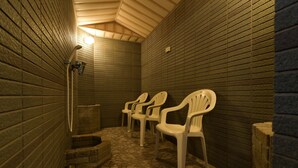 A small, enclosed bathroom with tiled walls and floor, a shower area, and three white plastic chairs. - Refre Forum (Tokyo)