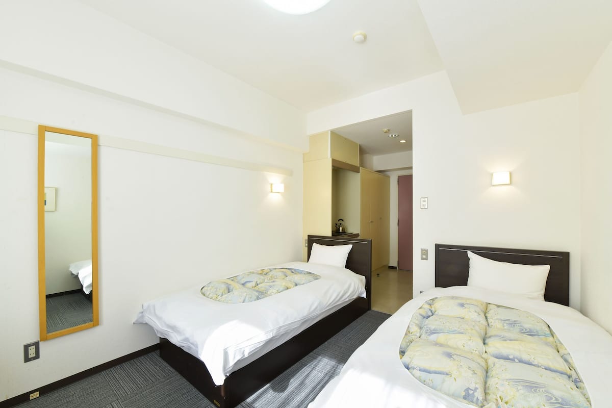 A hotel room with two single beds, a large mirror, and a small bedside table.