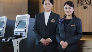 Two individuals standing in front of a reception desk with a sign that reads 'Press Inn.' - Keio Presso Inn Kudanshita (Tokyo)