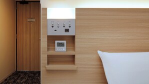 A hotel room with a wooden headboard, a bedside table with a clock, and a door to the left. - Keio Presso Inn Kudanshita (Tokyo)