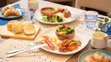 Mesa de café da manhã com pratos de comida, incluindo ovos, bacon e vegetais, juntamente com croissants e café.