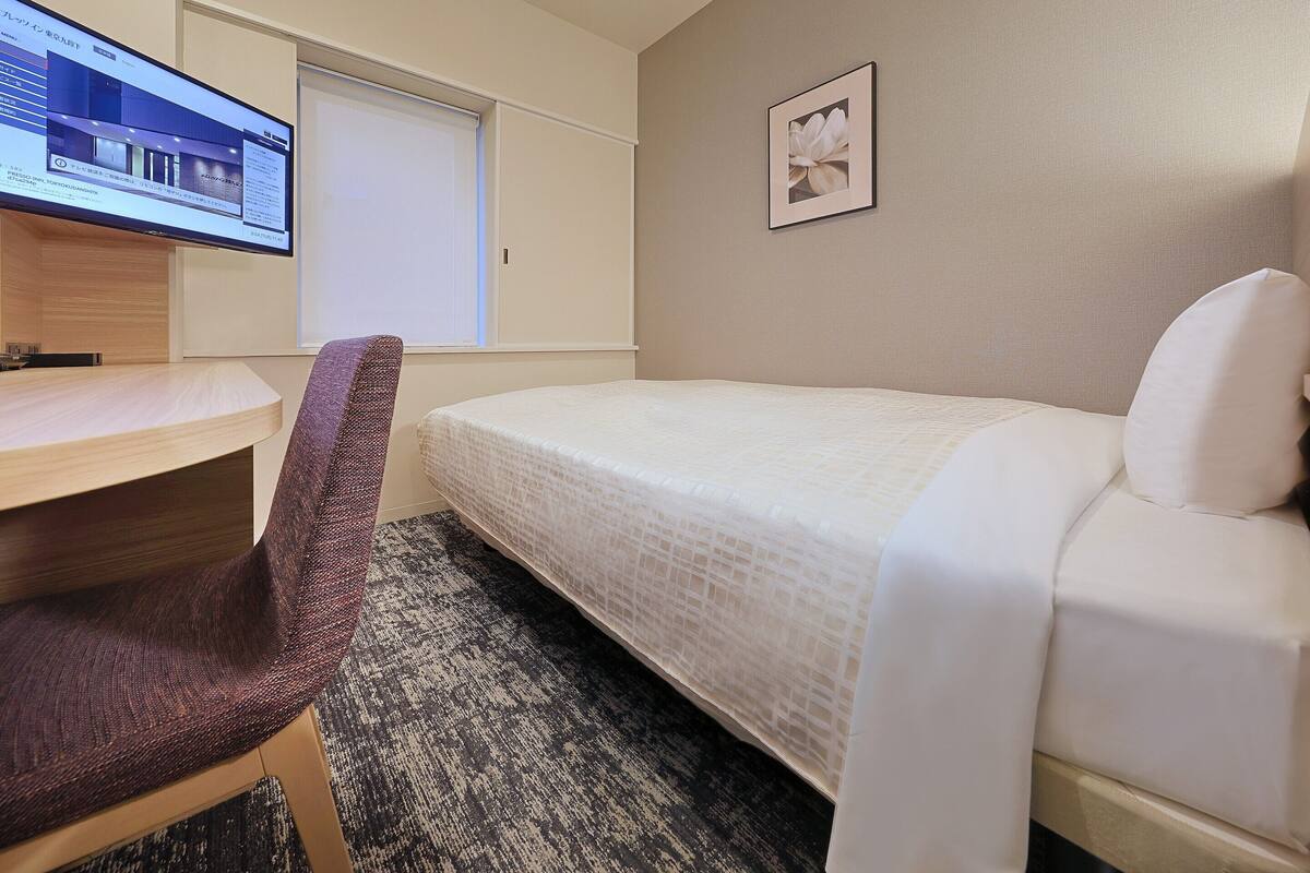 A hotel room with a bed, a desk, a chair, a TV, and a framed picture on the wall.