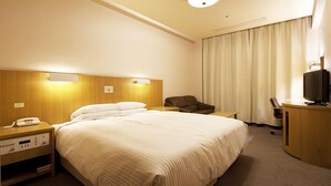 Ett hotellrum med en stor säng, sängbord, ett skrivbord med en stol, en tv och gardiner.