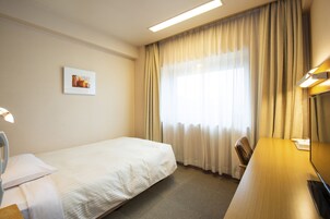 A hotel room with a single bed, a desk, a chair, a flat-screen TV, and a window with curtains.