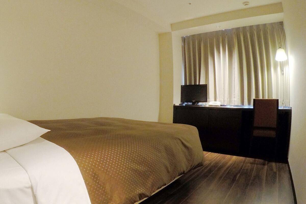 A hotel room with a bed, a desk, a chair, a TV, and a window with curtains.