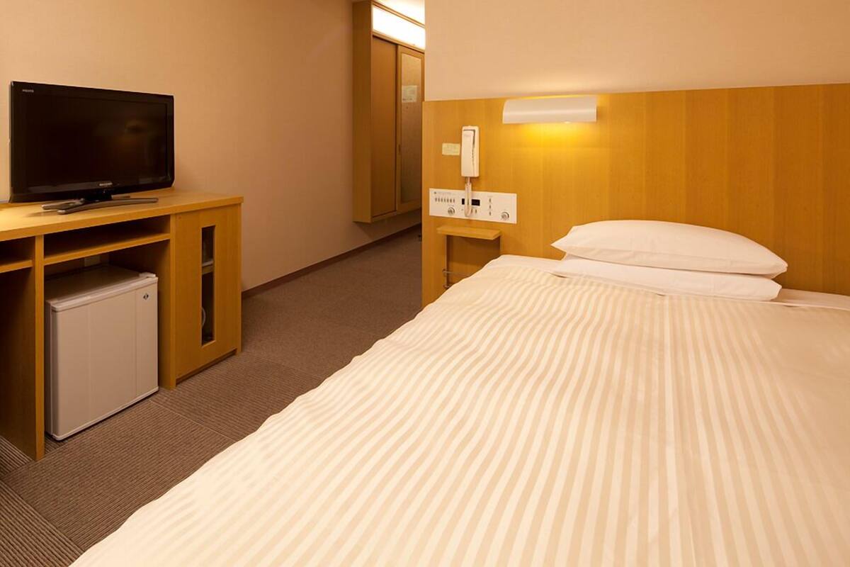 A hotel room with a bed, a television, a mini-fridge, a desk, and a wardrobe.