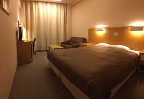 Una habitación de hotel con una cama grande, un escritorio, una silla y una lámpara de escritorio.