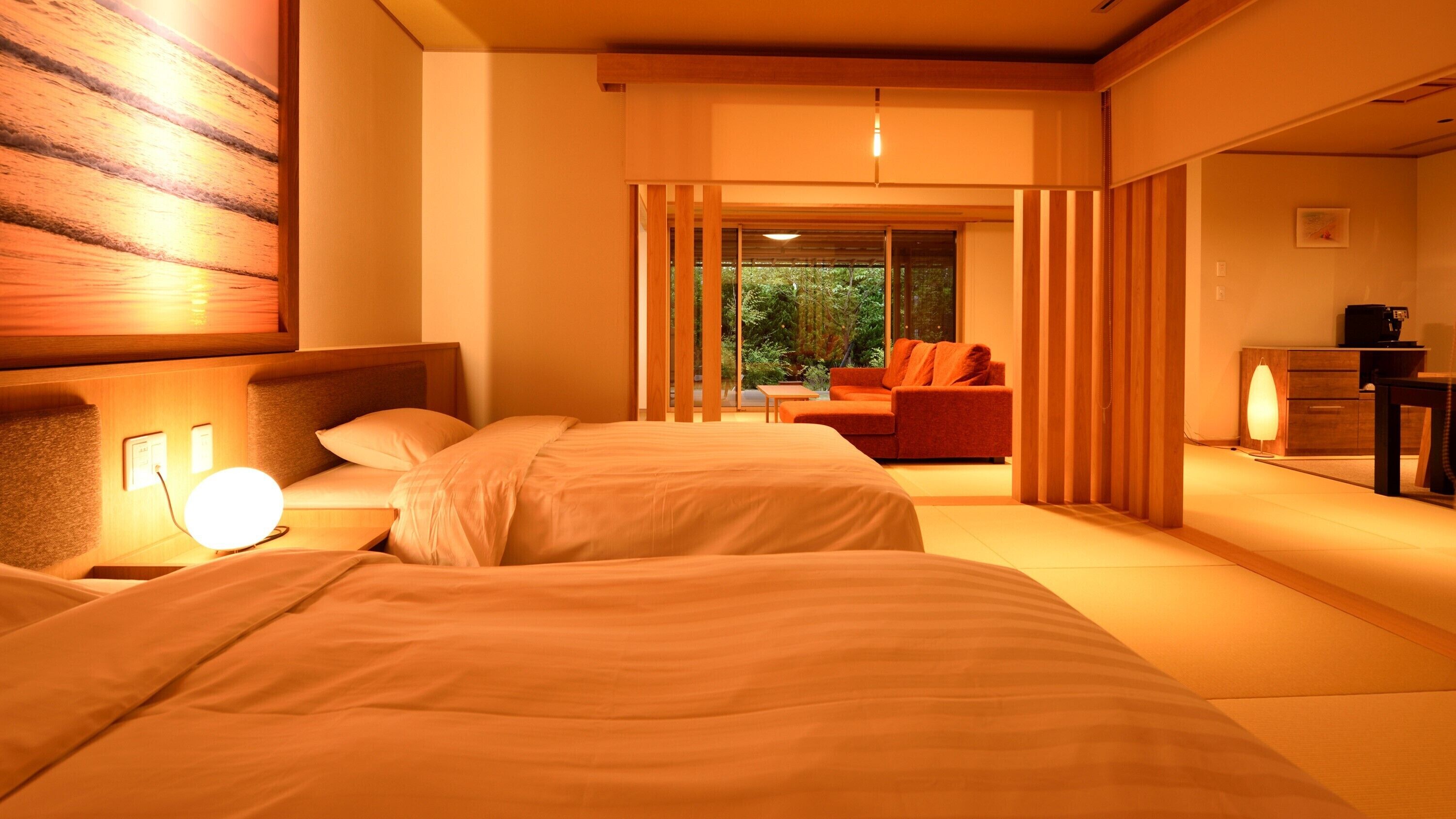 Habitación de hotel con dos camas, una zona de estar con sofá y mesa, y vistas a zonas verdes.