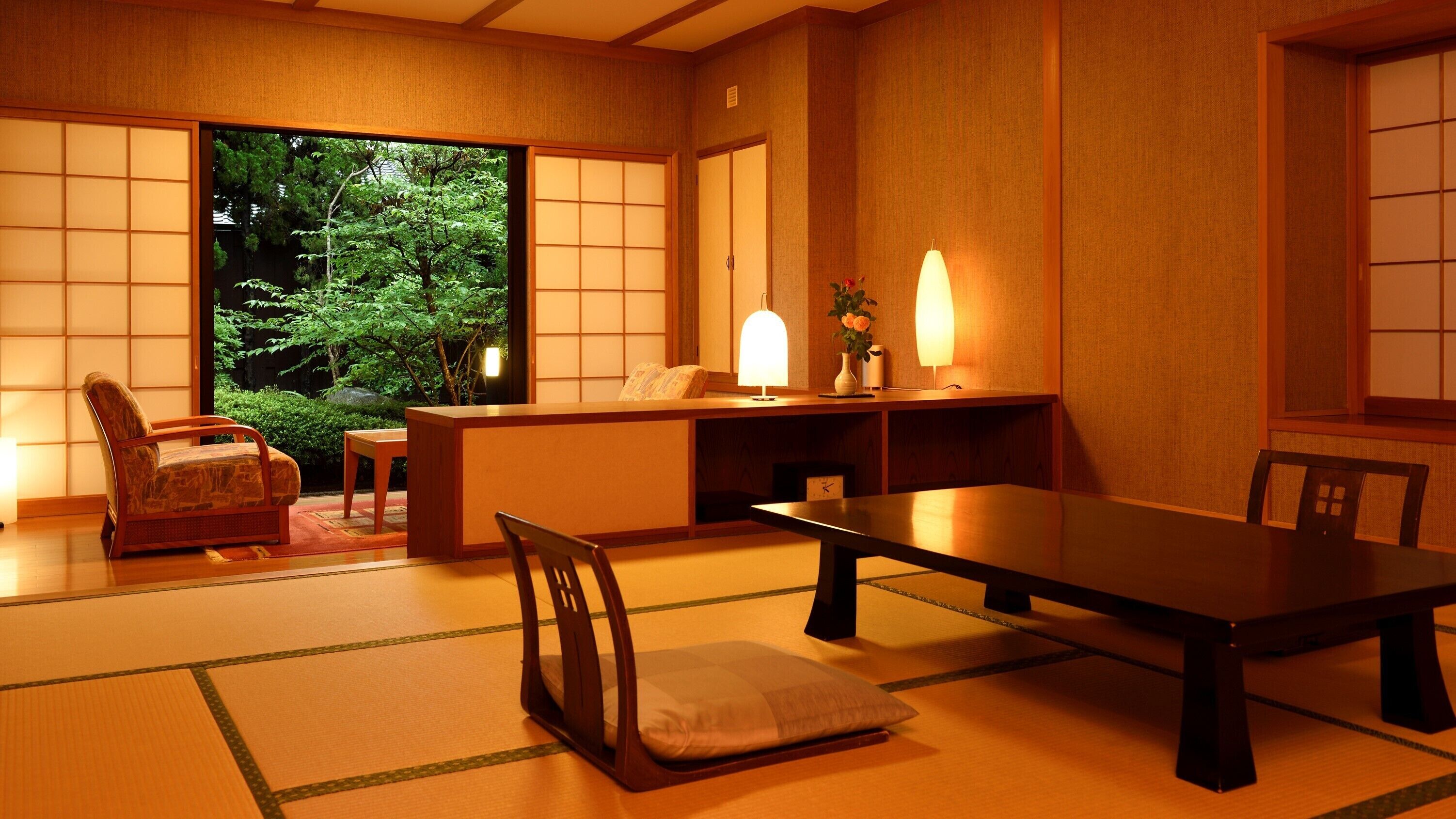 Una habitación japonesa tradicional con suelo de tatami, una mesa baja, sillas y puertas correderas.