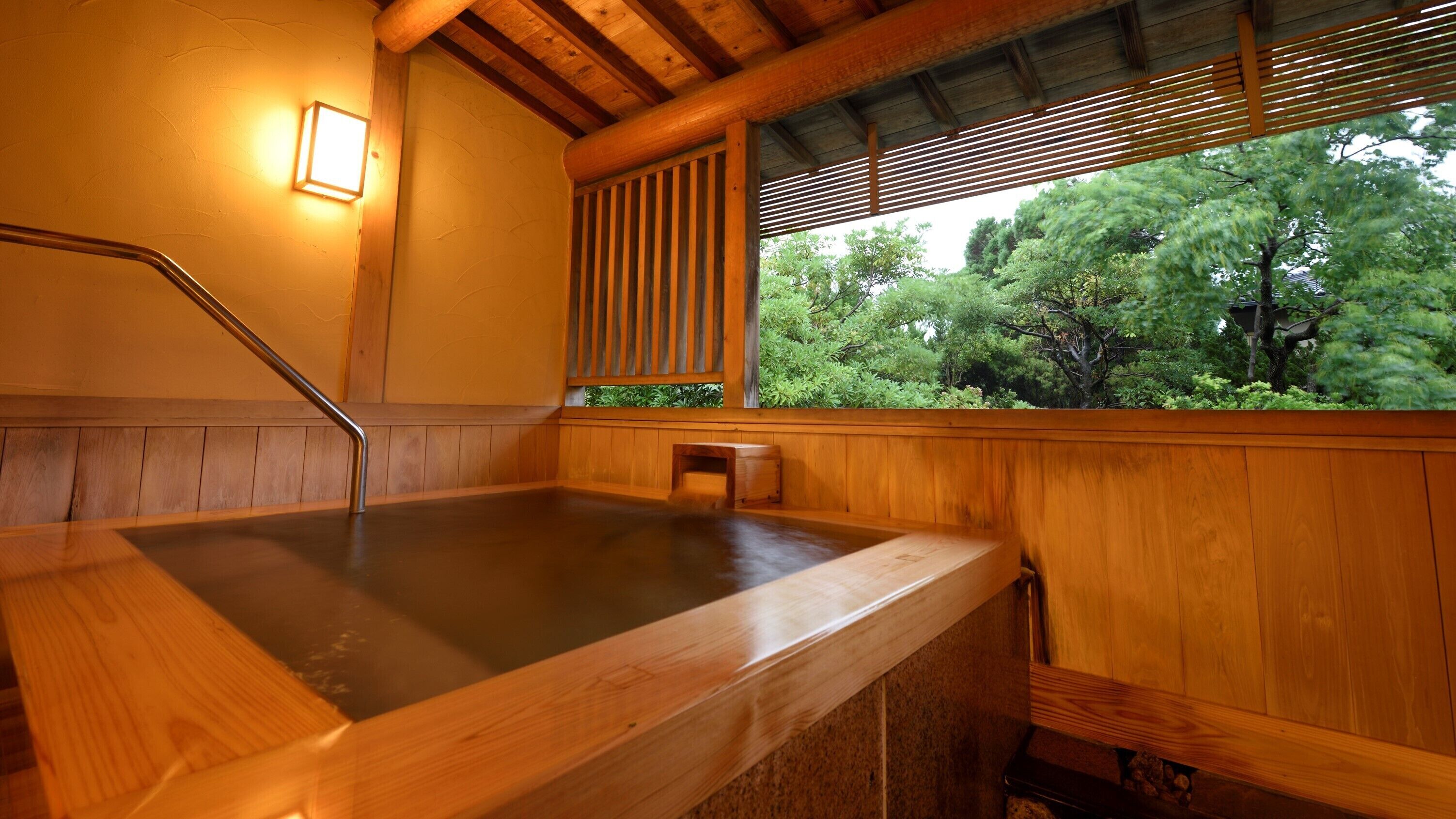 Un jacuzzi de madera con un banco, un mueble de madera pequeño y una ventana que da a las copas de los árboles.