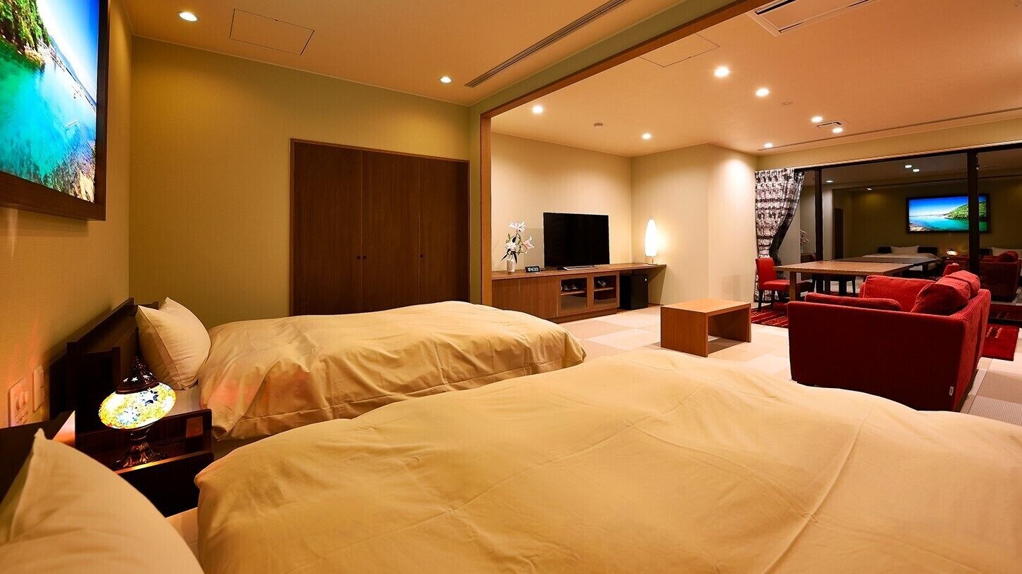 Habitación de hotel con dos camas, televisión, escritorio, silla y vista a la playa.