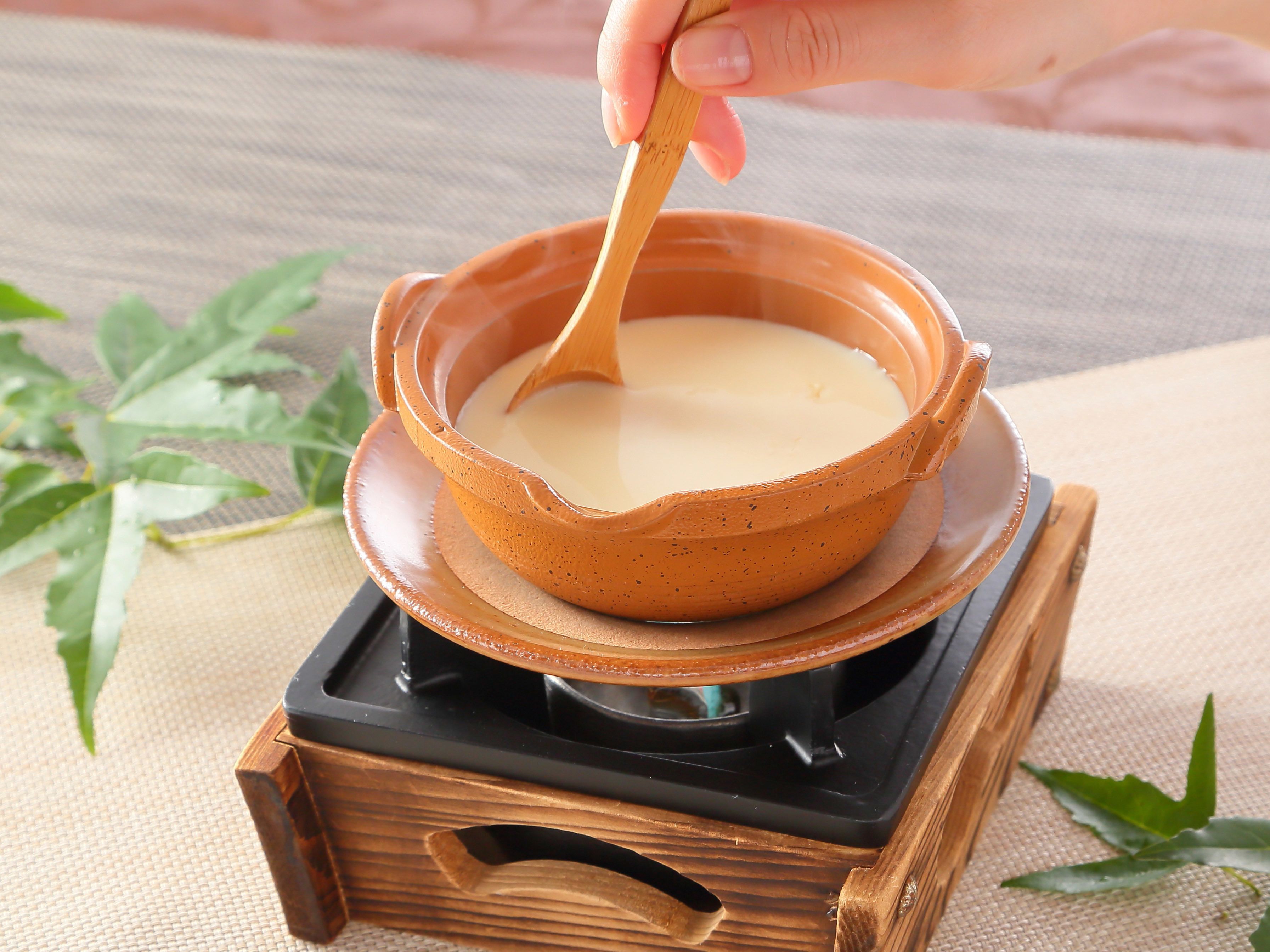A traditional clay pot on a stove with a wooden handle, placed on a woven mat.
