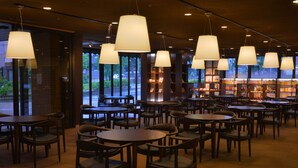 A restaurant with multiple tables and chairs, large hanging lamps, and a view of the outside through large windows.