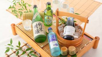 A wooden tray with various bottles and glasses, including a green bottle with Japanese characters, a blue bottle labeled "STARS Pure," and a wooden bucket with a bottle of sparkling wine.