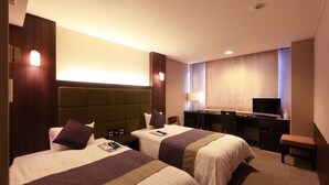 A hotel room with two beds, a desk, a chair, a television, and a lamp.