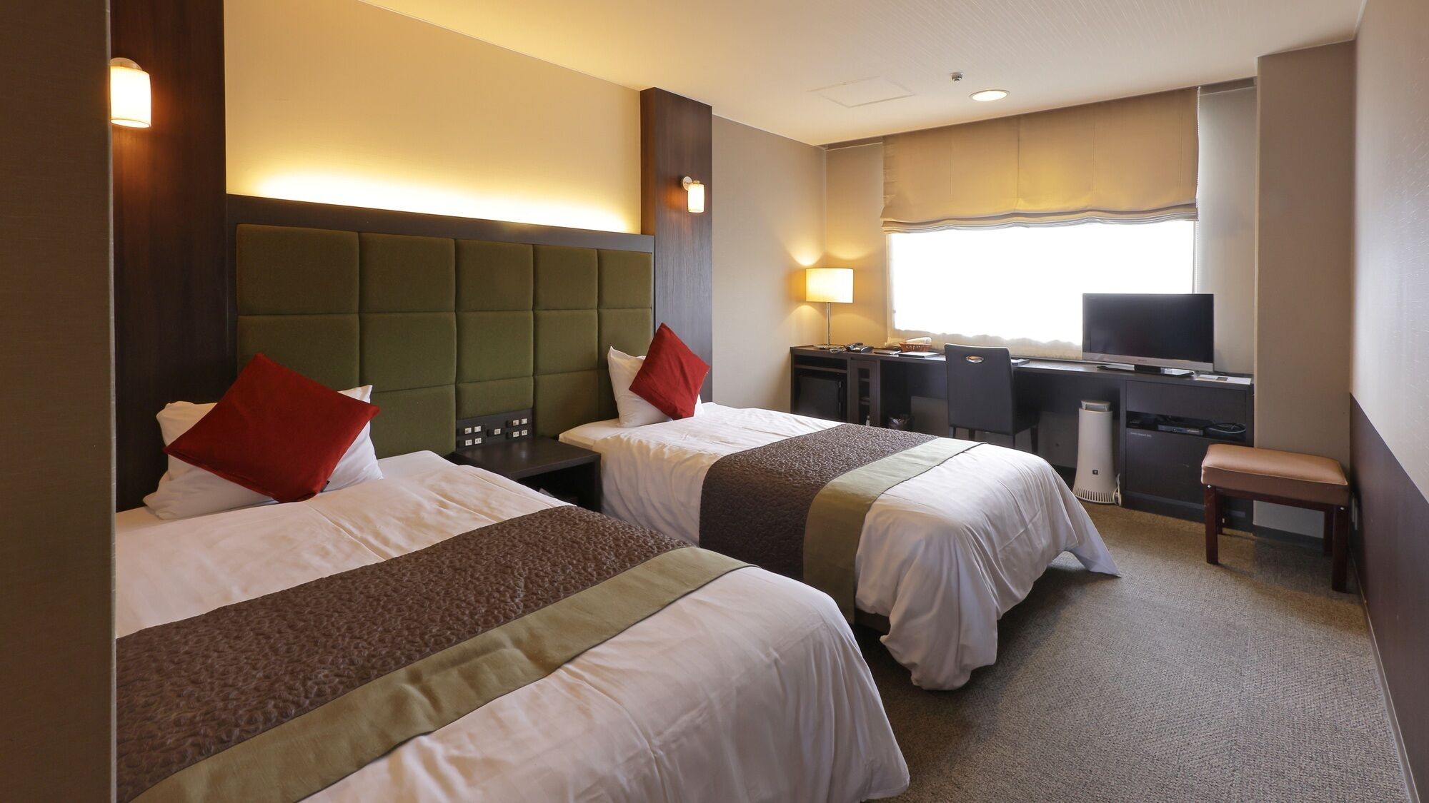 A hotel room with two beds, a desk, a chair, and a television.