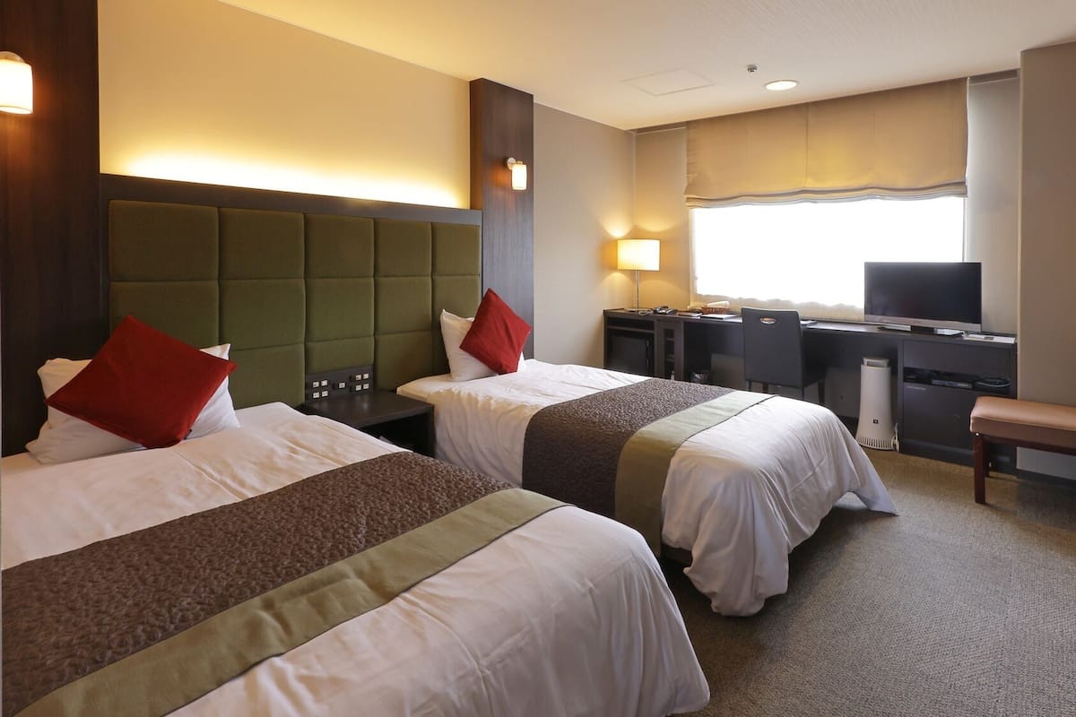 A hotel room with two beds, a desk, a chair, and a television.