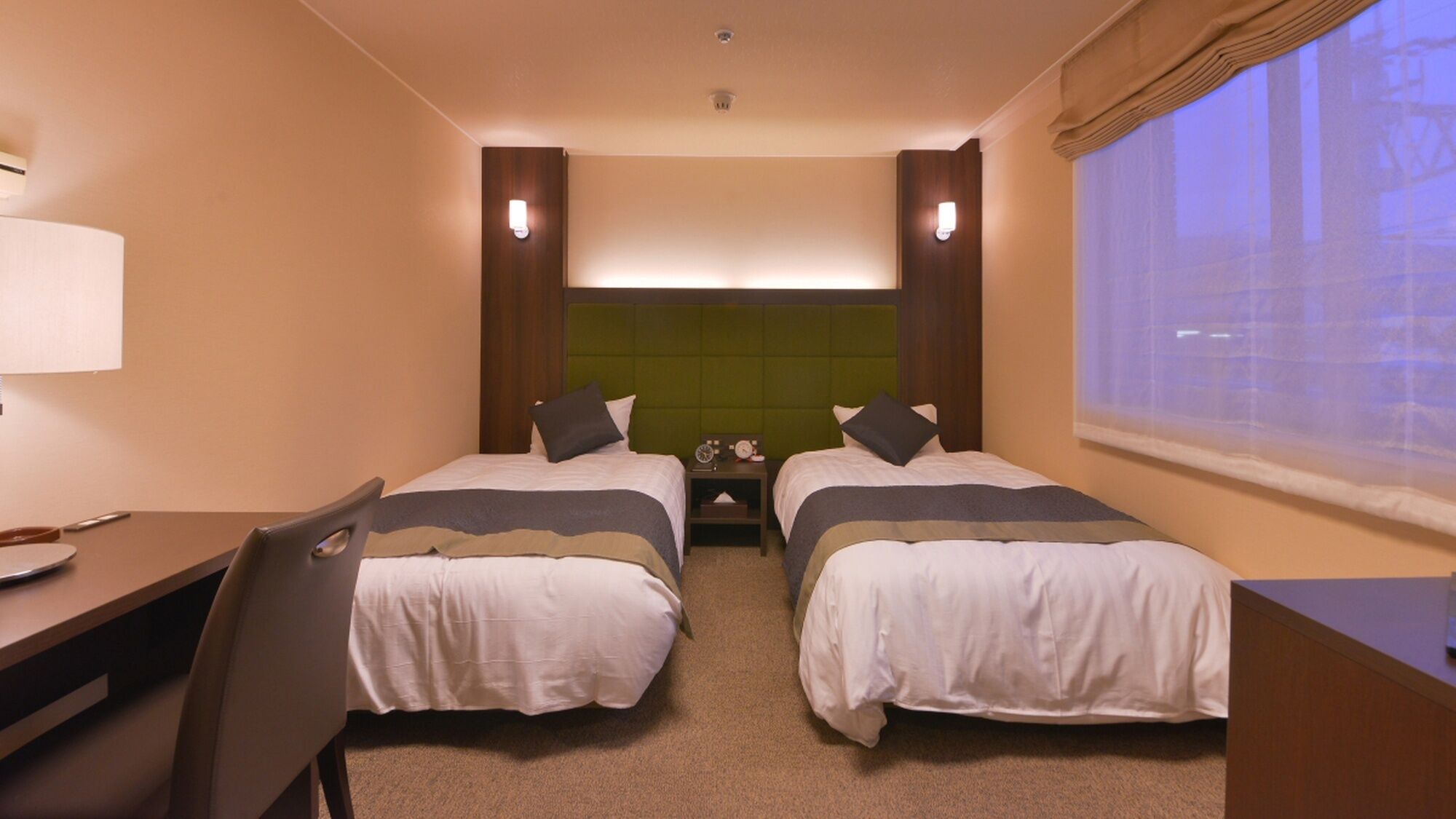 A hotel room with two beds, a desk, a chair, a nightstand, and a window with a view.