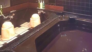 A bathroom with a black bathtub, two sinks, and a mirror.