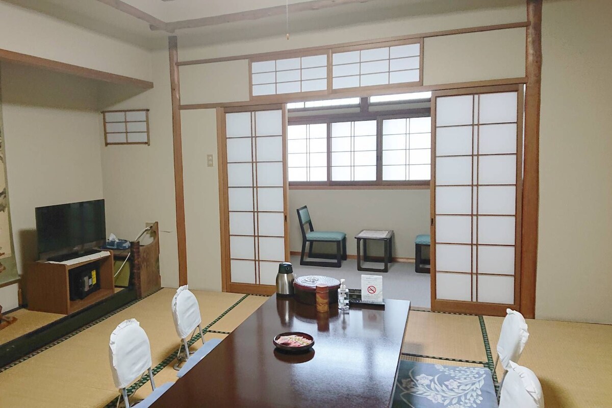 A traditional Japanese-style room with tatami flooring, a low table with a TV, and sliding shoji doors.