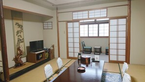 A traditional Japanese-style room with tatami flooring, a low table with a tea set, a television, and sliding doors. - Kagetsu Ryokan (Maizuru)