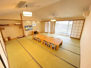 A tatami mat room with a wooden table and chairs, a television, and sliding doors. - Hotel The Day Osaka (Osaka)
