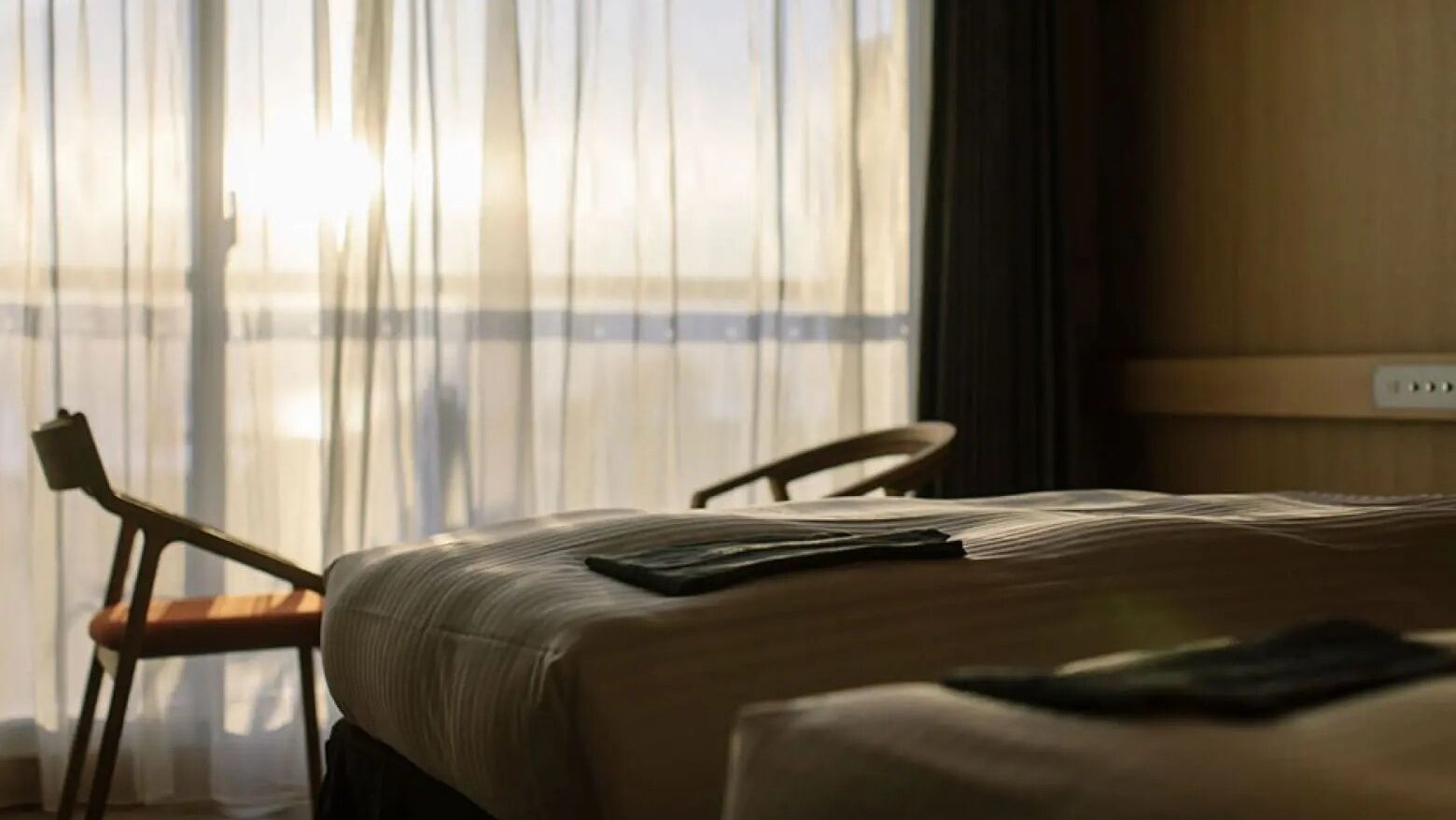 Quarto de hotel com cama, uma cadeira e janela com cortinas.