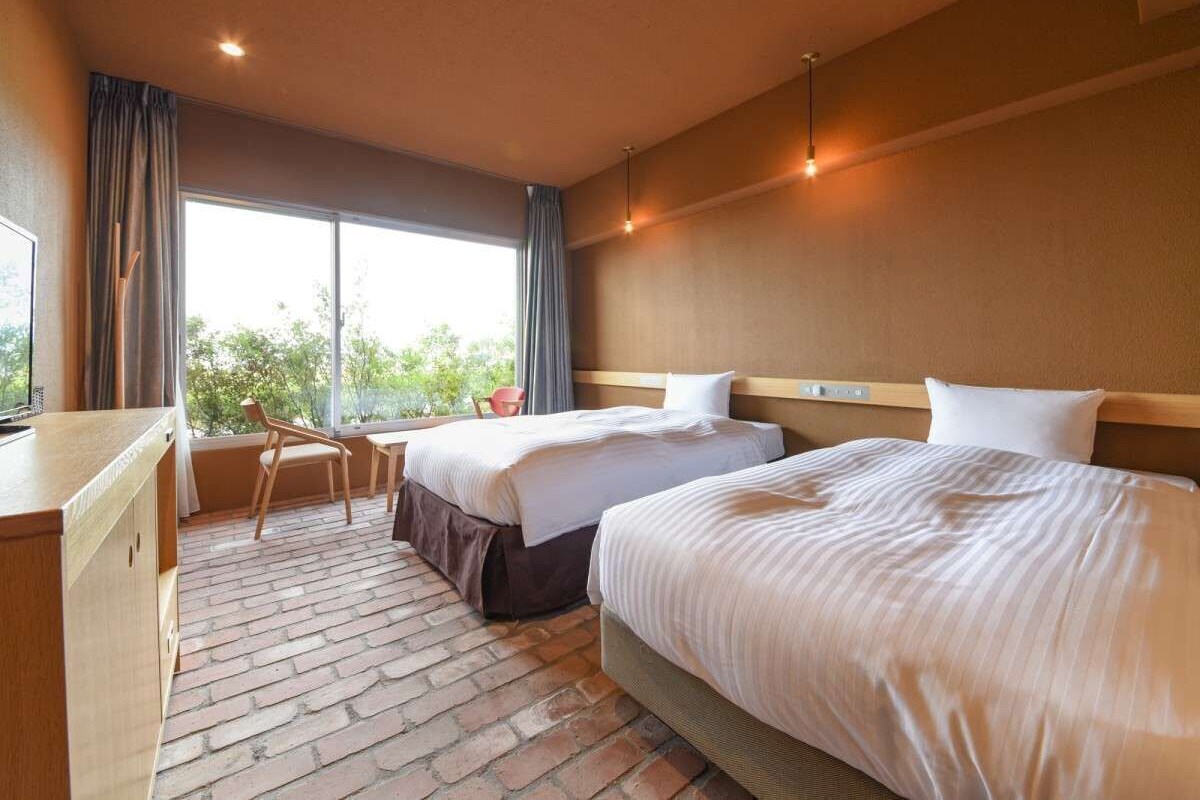 A hotel room with two beds, a desk, and a chair.