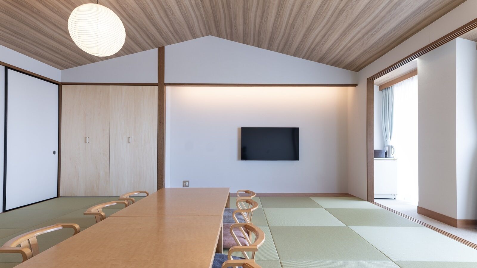 Uma sala de conferência com uma mesa comprida, cadeiras, uma televisão e portas deslizantes.