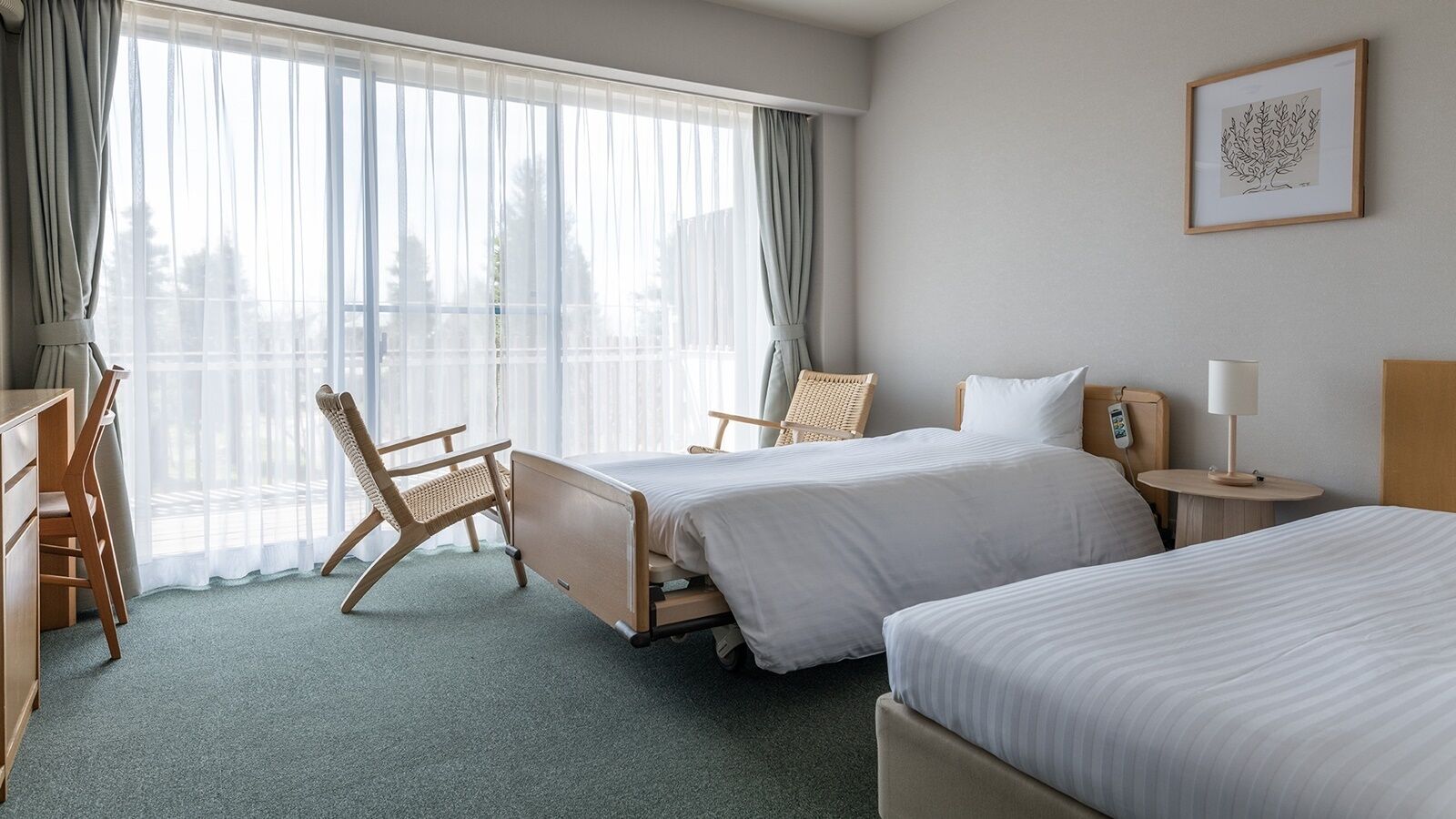 Quarto de hotel com duas camas, uma escrivaninha, uma cadeira, mesa de cabeceira com abajur e janela com cortinas.
