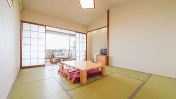 Een traditionele Japanse kamer met tatami vloerbedekking, een lage houten tafel en een schuifdeur naar een buitenbalkon.