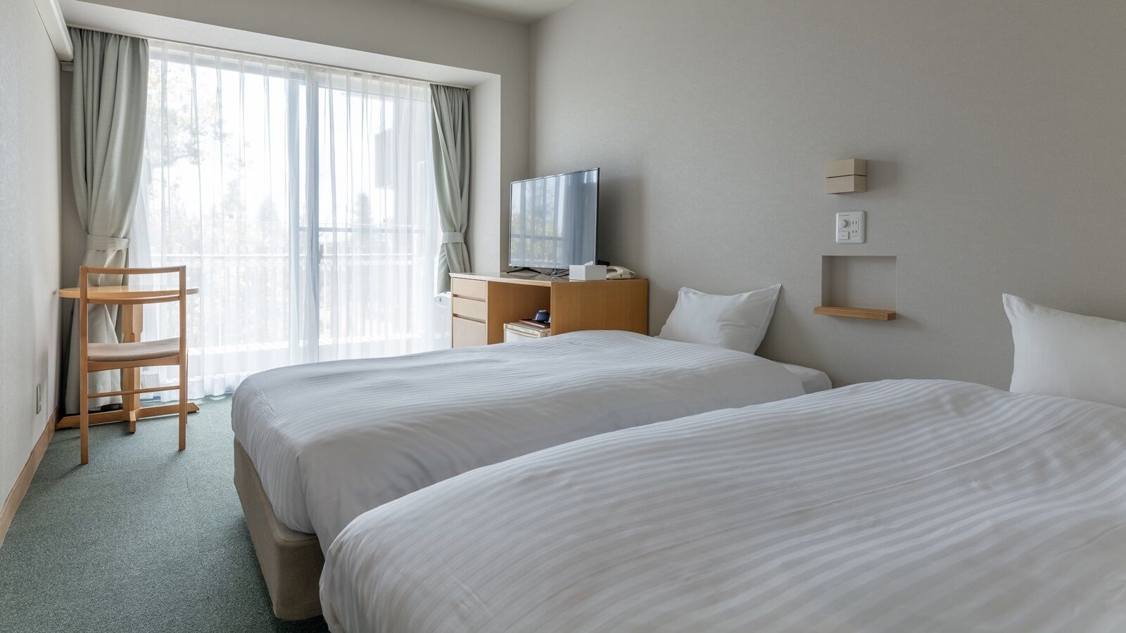 Quarto de hotel com duas camas, uma televisão, uma escrivaninha e uma cadeira.