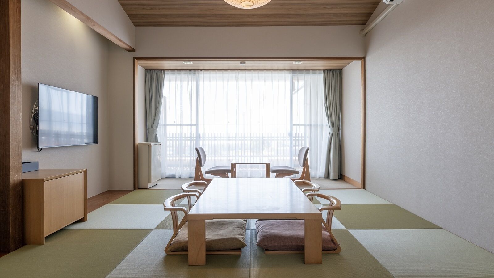 Um quarto em estilo tradicional japonês, com tatames no chão, uma mesa de madeira baixa e uma televisão na parede.