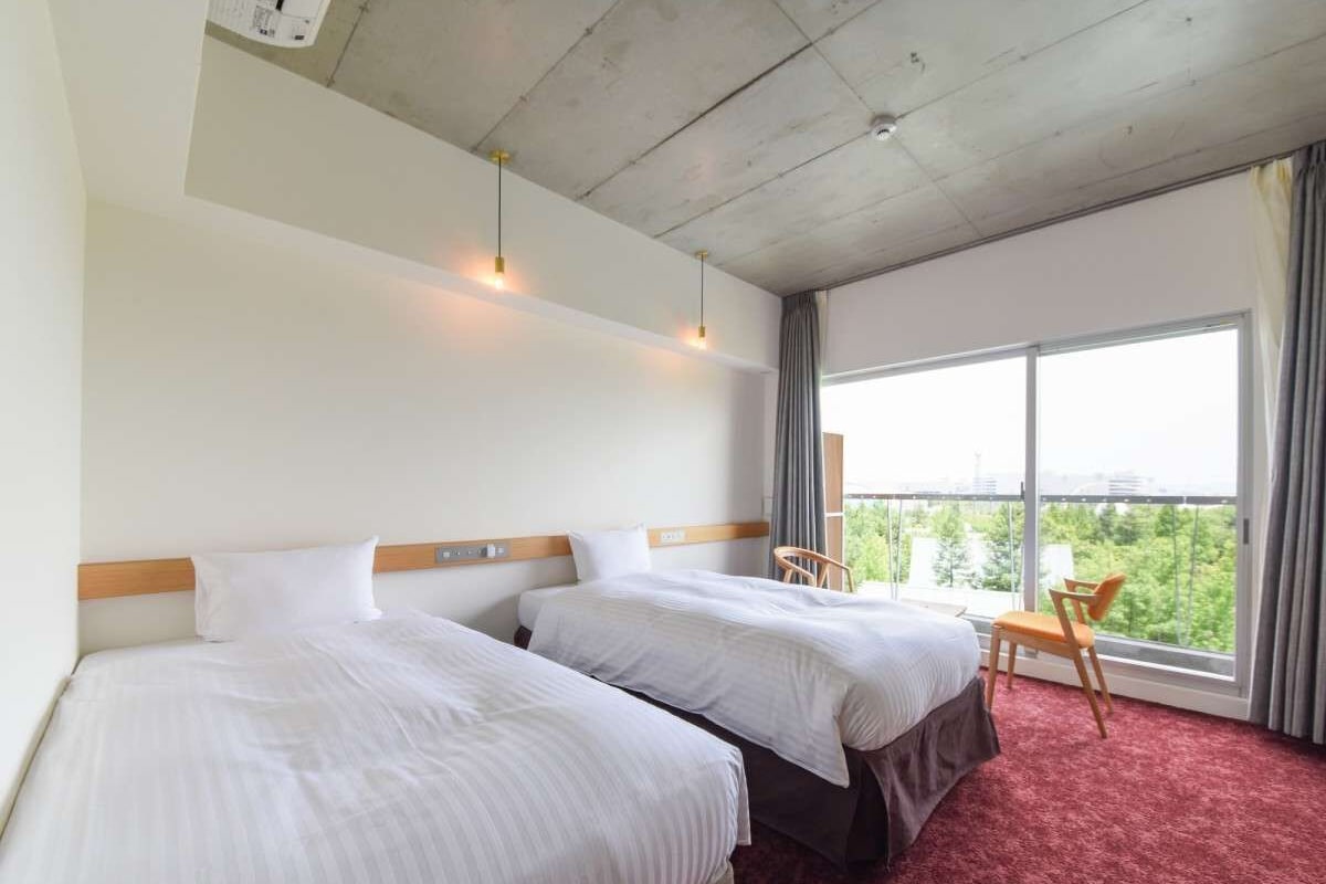 A hotel room with two beds, a large window with a view, and a red carpet.