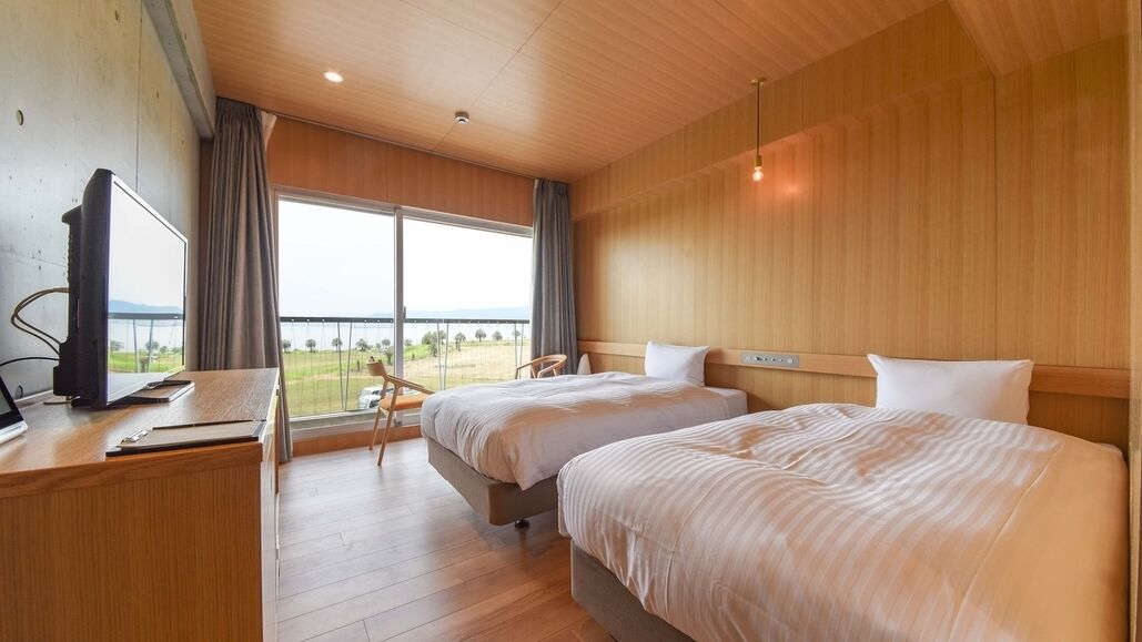 Quarto de hotel com duas camas, uma mesa de escritório com computador e uma janela grande com vista.