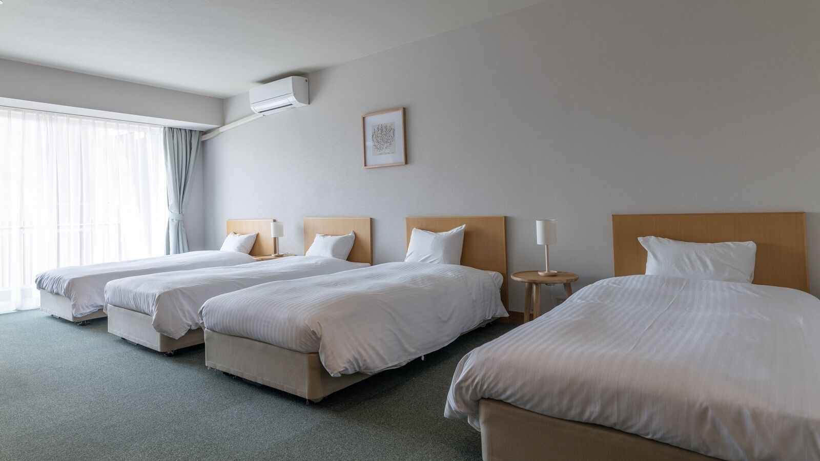 Quarto de hotel com três camas, ar condicionado no teto, quadro emoldurado na parede e janela com cortinas.