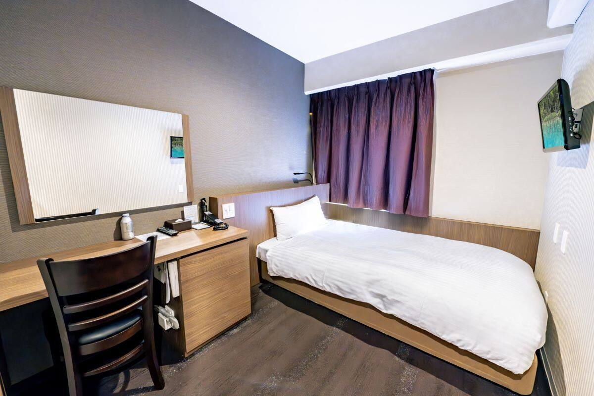 A hotel room with a bed, a desk, a chair, a mirror, and a window with curtains.