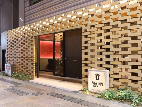A hotel entrance with a brick-patterned facade, a glass door, and a signboard displaying the hotel name. - JR WEST GROUP VIA INN UMEDA (Osaka)