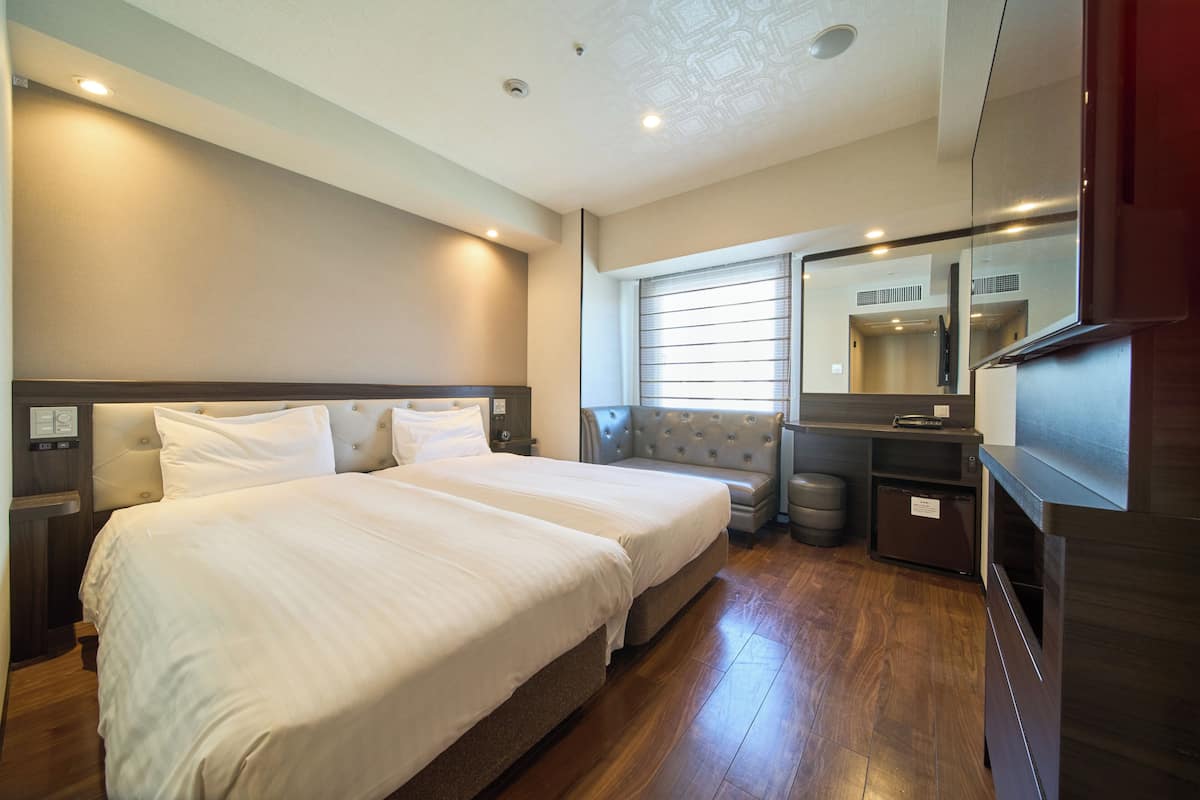 A hotel room with two beds, a vanity with a mirror, a small seating area, and a trash bin.