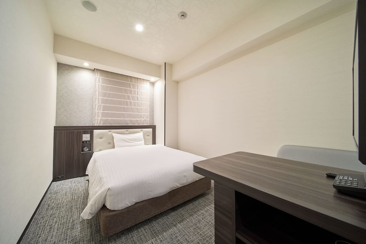 A hotel room with a bed, a desk, a chair, a television, and a window with blinds.