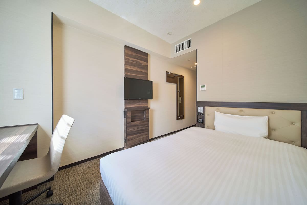 A hotel room with a bed, a desk, a chair, a television, and a door.