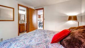 Quarto com colcha estampada, travesseiro vermelho e abajur.