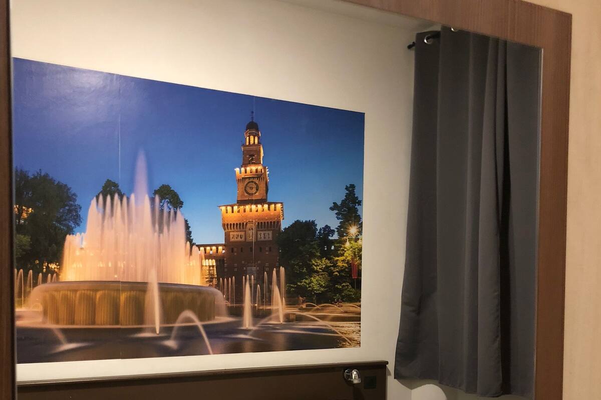 A hotel room with two beds, a large mirror reflecting a fountain and clock tower, and a dark curtain.