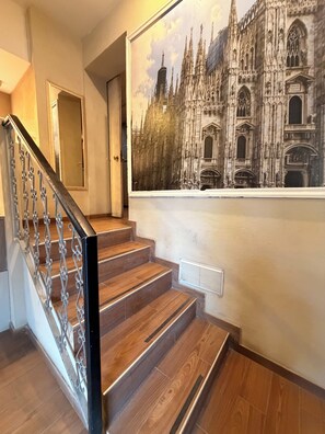 A staircase with wooden steps and metal railings, leading to a room with a large mural of a cathedral.