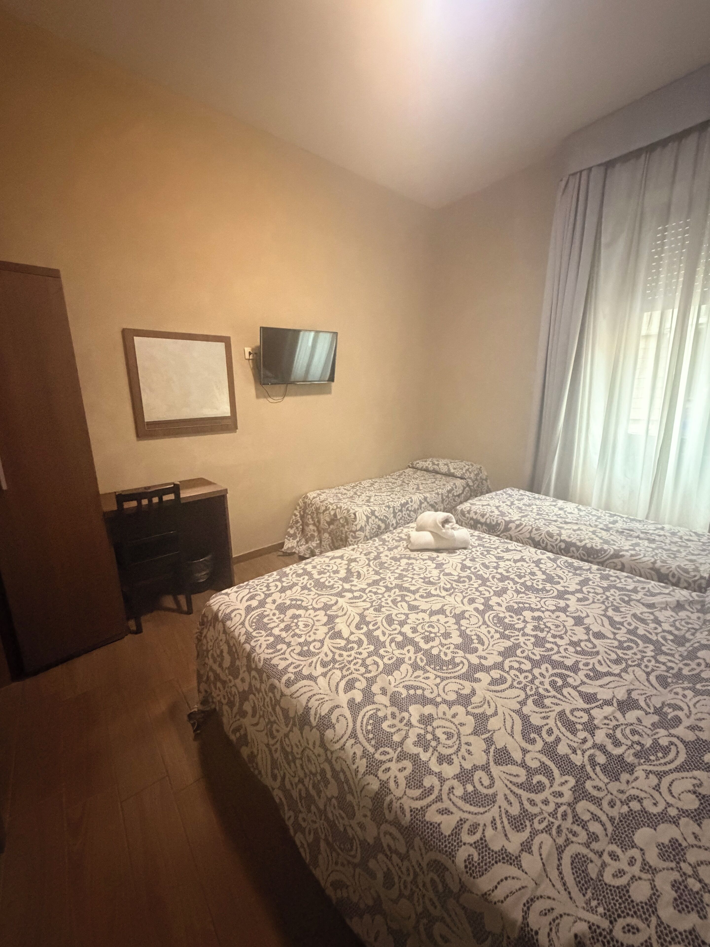 Een hotelkamer met twee bedden, een televisie, een dressoir en een raam met gordijnen.
