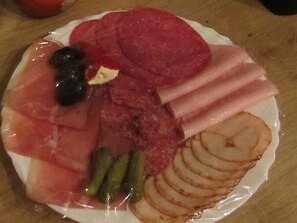Un plato con diferentes alimentos, entre ellos, jamón en rodajas, pepinillos y una rebanada de manzana.