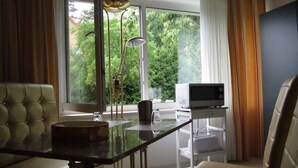 Ein modernes Wohnzimmer mit Glastisch, Sofa, Fernseher und Blick auf Grünflächen.